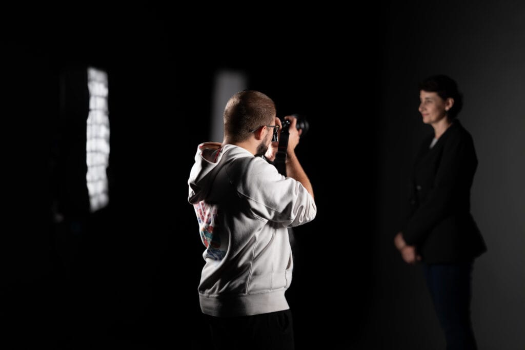 Fotograf w bluzie fotografuje kobietę na czarnym tle